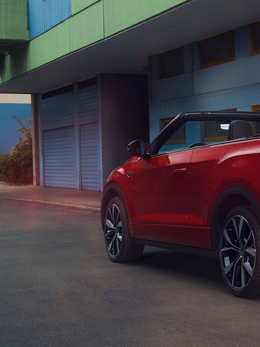 Ansicht des Hecks eines roten T-Roc Cabriolet mit geöffnetem Dach, parkend am Straßenrand. 