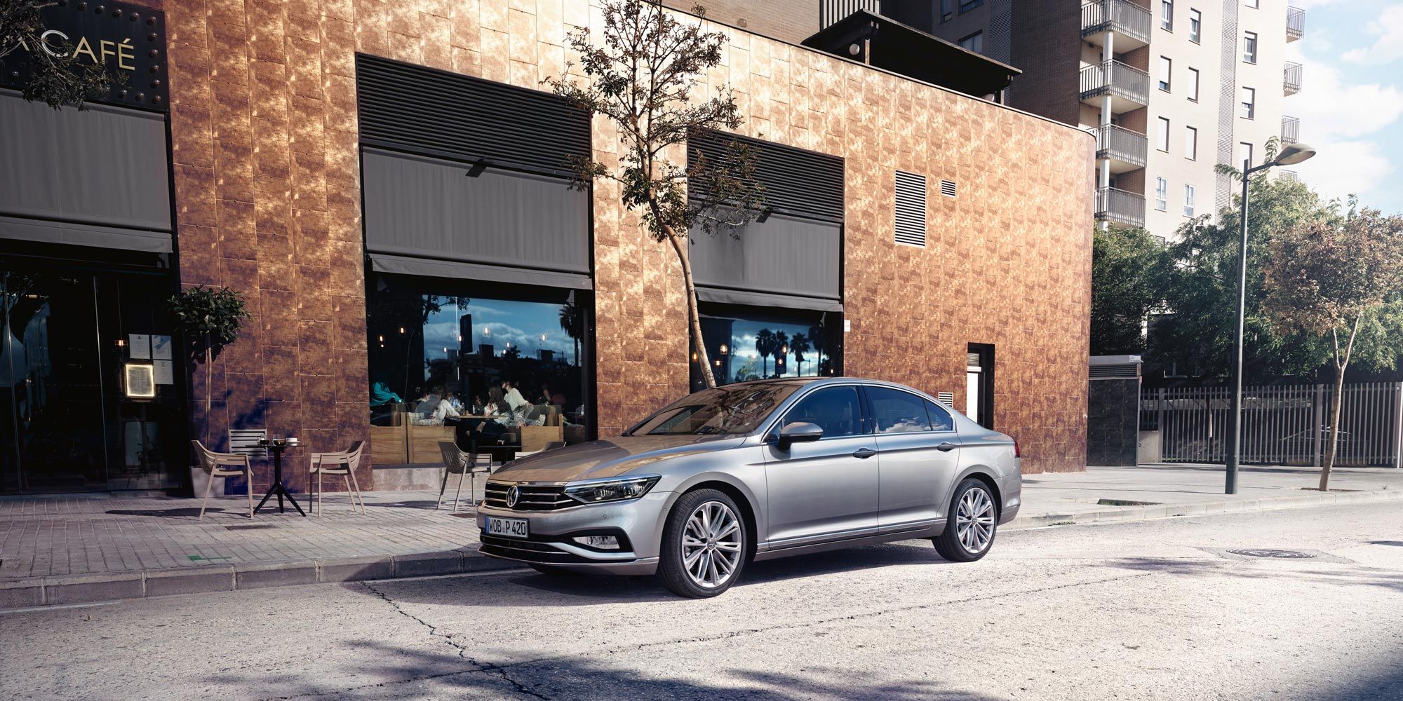 Сребрист Volkswagen Passat паркиран пред кафене в градска среда