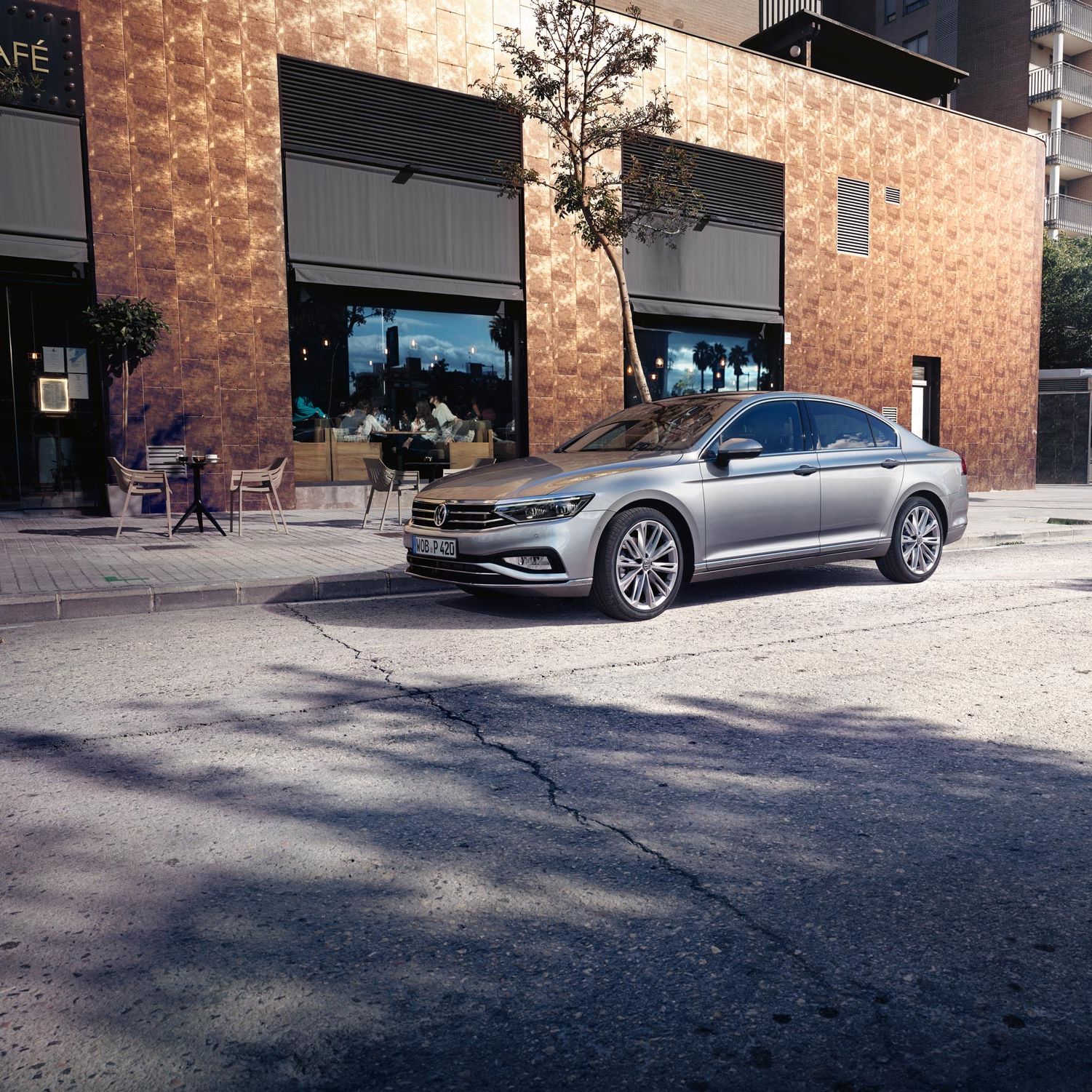 Сребрист Volkswagen Passat паркиран пред кафене в градска среда