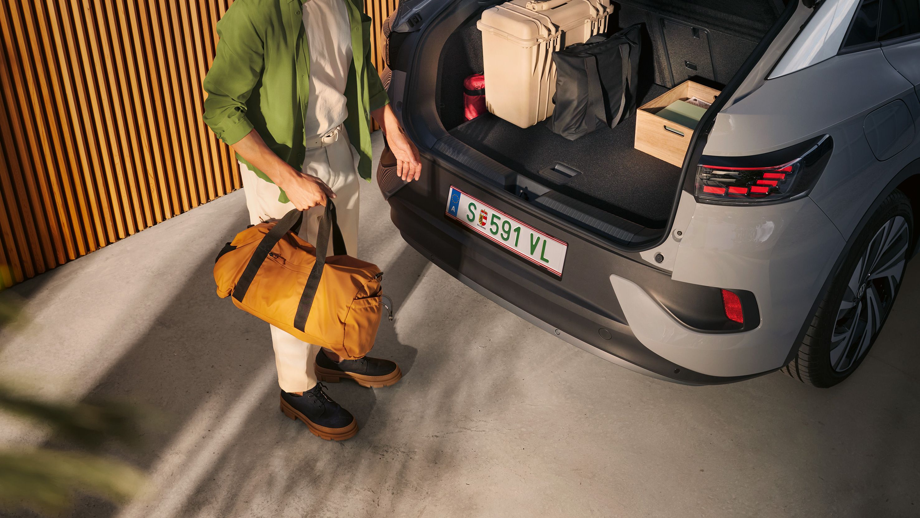 VW ID.5 mit geöffnetem Kofferraum und Gepäck darin, unter der offenen Heckklappe steht ein Mann mit einer Tasche in der Hand