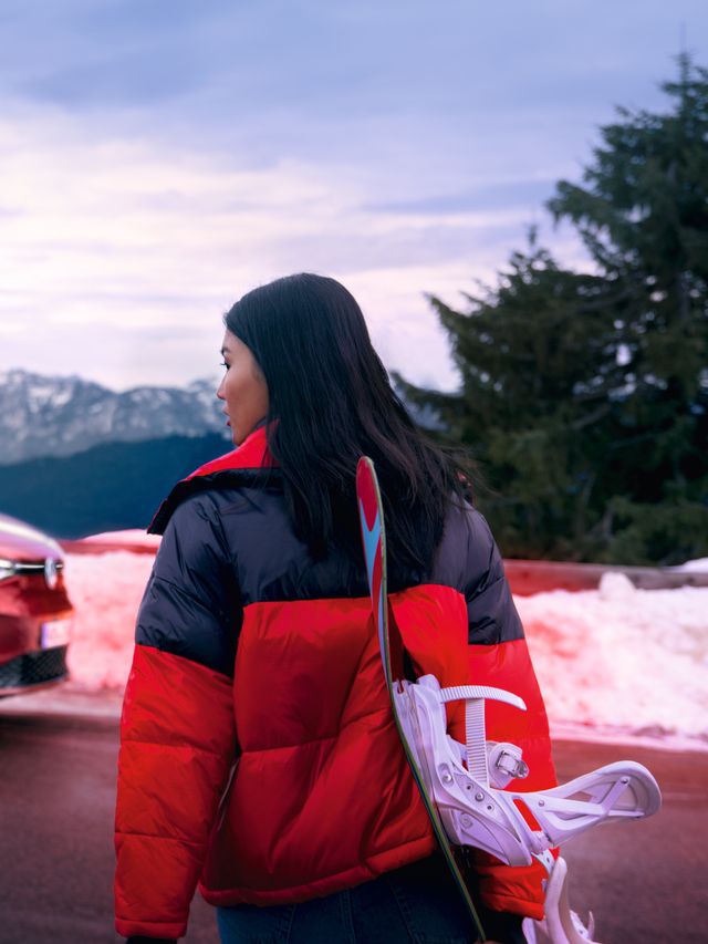 Страничен изглед на червен VW ID.4 GTX на планински фон, на преден план жена гледа към автомобила
