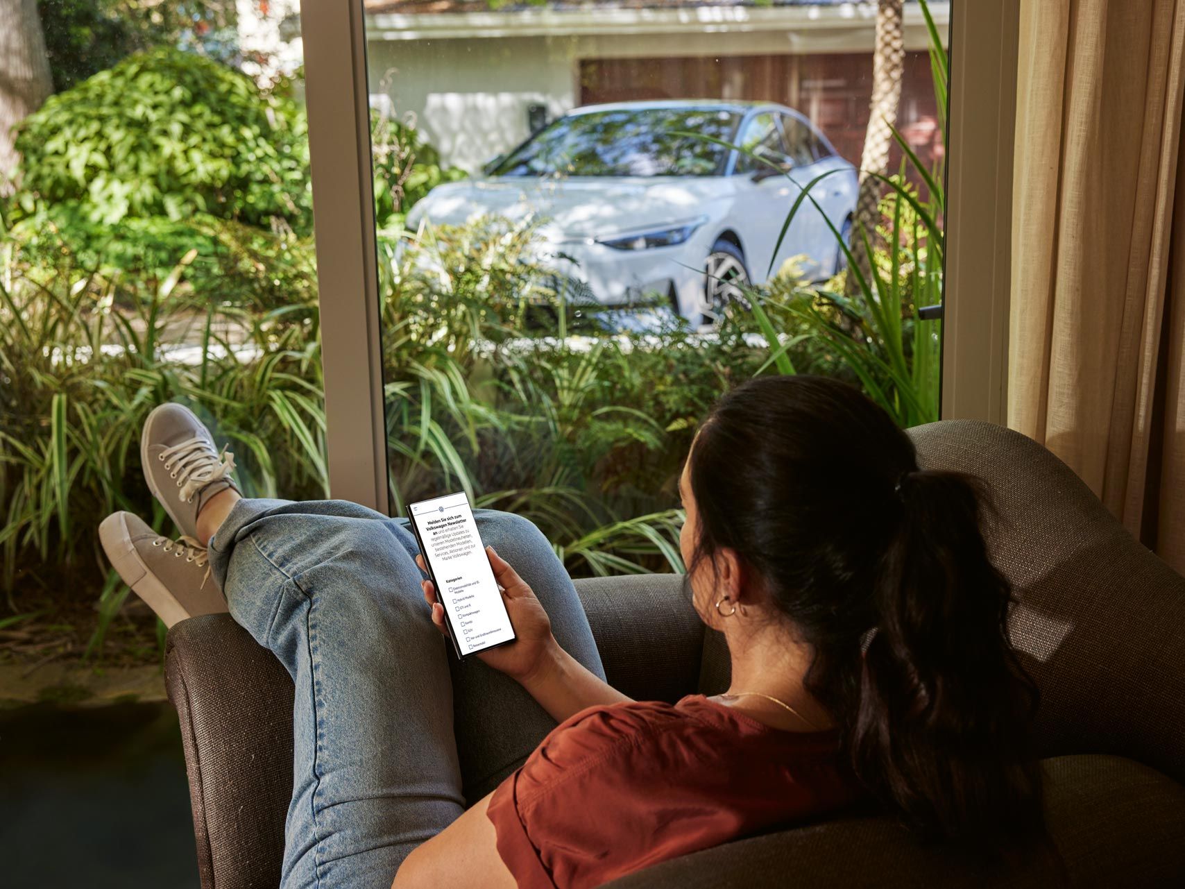 Eine Frau sitzt entspannt im Sofa und blickt auf ihr Smartphone