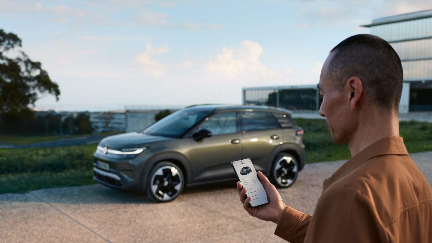 Зелен VW ID.Cross е паркиран пред жилищна сграда, до него стои мъж, който гледа смартфона си.