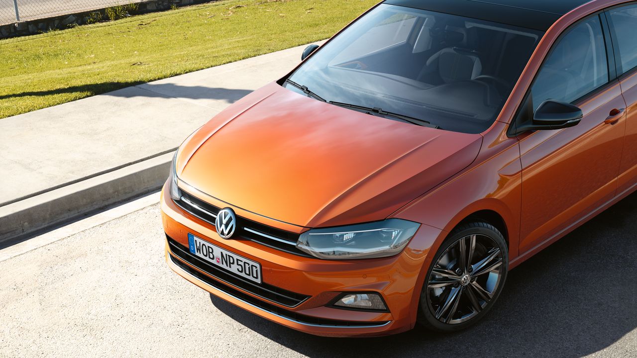 Оранжев Volkswagen Polo с черен покрив, паркиран на слънчев път