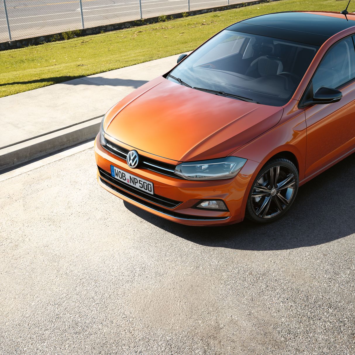 Оранжев Volkswagen Polo с черен покрив, паркиран на слънчев път