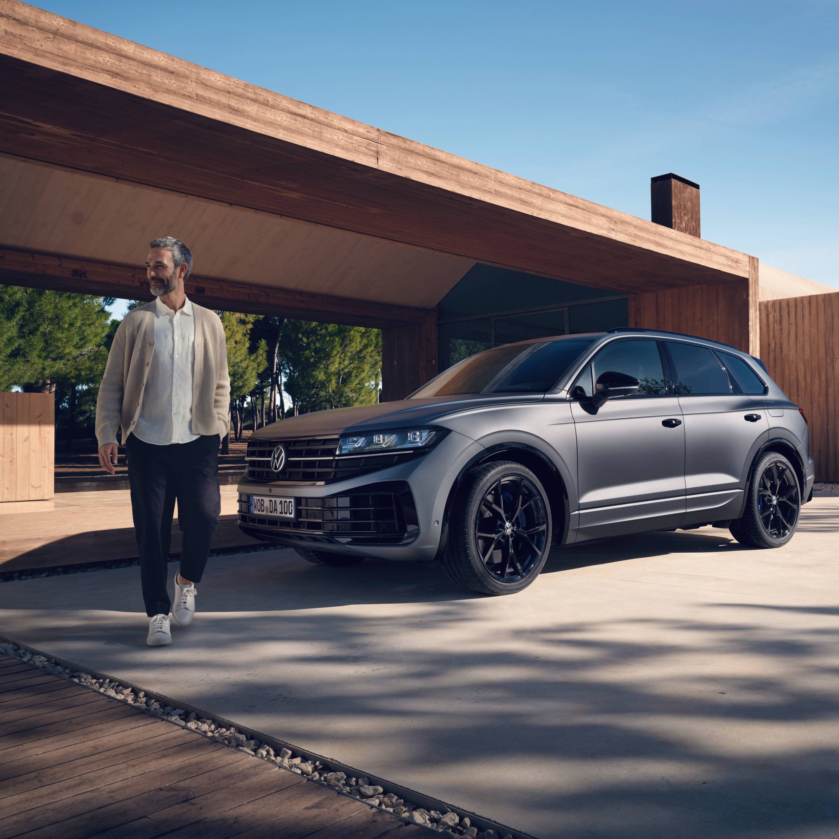 Volkswagen Touareg паркиран пред модерен дом с мъж, излизащ навън