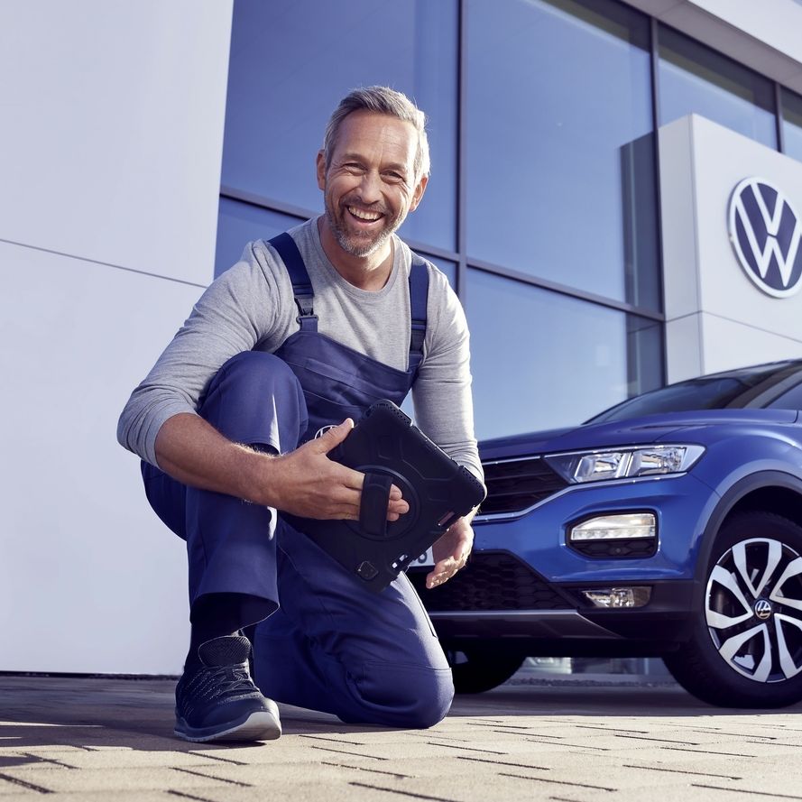 Автомобилен техник пред дилър на Volkswagen, усмихнат до син Volkswagen T-Roc.